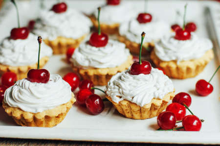 Beautiful chocolate cupcakes with white protein cream and cherry. Vanilla cupcakes with  cream frosting and a cherry on top. Cherry Cupcake Shot on wooden table. Ripe red cherries and currant muffinの写真素材
