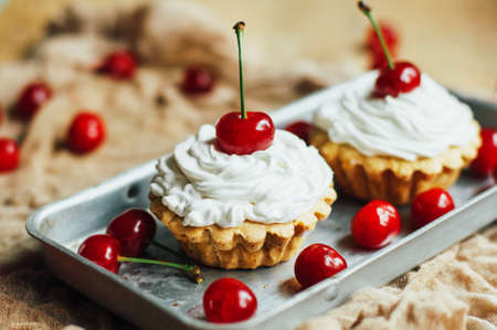 Beautiful chocolate cupcakes with white protein cream and cherry. Vanilla cupcakes with  cream frosting and a cherry on top. Cherry Cupcake Shot on wooden table. Ripe red cherries and currant muffinの写真素材