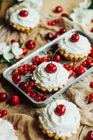 Beautiful chocolate cupcakes with white protein cream and cherry. Vanilla cupcakes with  cream frosting and a cherry on top. Cherry Cupcake Shot on wooden table. Ripe red cherries and currant muffinの写真素材