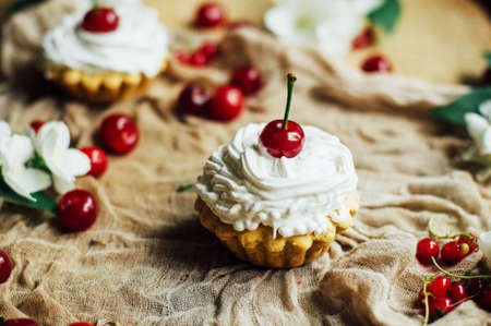 Beautiful chocolate cupcakes with white protein cream and cherry. Vanilla cupcakes with  cream frosting and a cherry on top. Cherry Cupcake Shot on wooden table. Ripe red cherries and currant muffinの写真素材