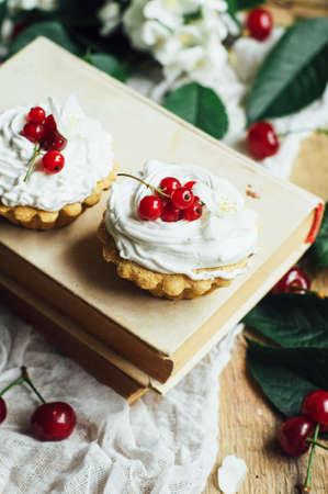 Beautiful chocolate cupcakes with white protein cream and cherry. Vanilla cupcakes with  cream frosting and a cherry on top. Cherry Cupcake Shot on wooden table. Ripe red cherries and currant muffinの写真素材