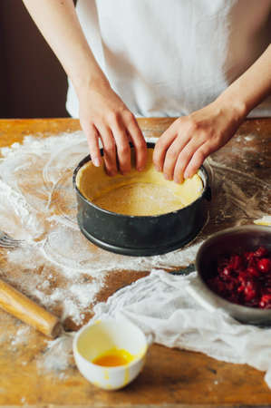 Ingredients for baking cake stuffed with fresh cherry pie. Female preparing cherry pie. Rustic dark style. See series recipe step on step. Womans hands. Recipe for homemade pie on short pastryの写真素材