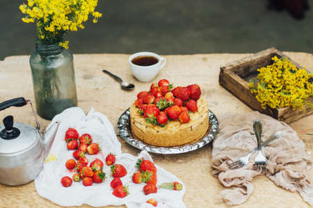 Woman eating a delicious home-made cake with aisheny and stuffed strawberries for dessert. Summer Styled dinner table. Coffee to the cake. sitting at the rustic dining tableの写真素材