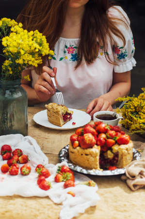 Woman eating a delicious home-made cake with aisheny and stuffed strawberries for dessert. Summer Styled dinner table. Coffee to the cake. sitting at the rustic dining tableの写真素材