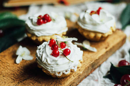 Beautiful chocolate cupcakes with white protein cream and cherry. Vanilla cupcakes with  cream frosting and a cherry on top. Cherry Cupcake Shot on wooden table. Ripe red cherries and currant muffinの写真素材