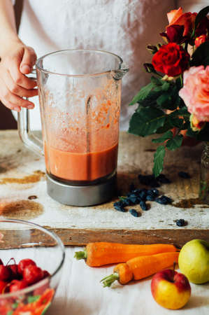 Hands makes strawberry smoothies in wooden table . Fresh strawberry smoothies fruit. Recipe carrot-strawberry smoothie. Action. Rustic dark style. Clean eating breakfast concept.の写真素材