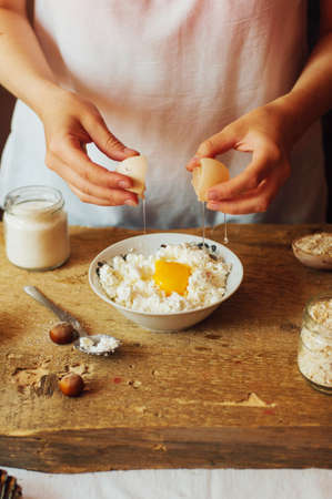 The woman in the kitchen prepares the curd pudding stuffed with ripe cherries. Recipe tvogozhnoy casserole with cherry. Country style dark. Women's hands. Home for the family cakeの写真素材
