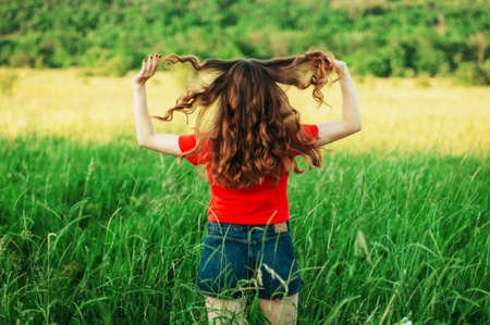 Young woman stay is burned field. Woman stands facing the camera and the visible light leak. Girl  standing in a green field. Portrait of a young beautiful girl on a background of natureの写真素材