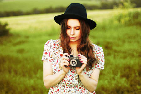 Retro photo camera woman with red hair. Portrait Of a Woman With Retro Camera. Smiling ginger-haired woman taking a photo with an old camera. Beautiful girl with curly hair holds an analog cameraの写真素材