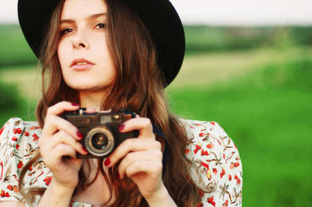 Retro photo camera woman with red hair. Portrait Of a Woman With Retro Camera. Smiling ginger-haired woman taking a photo with an old camera. Beautiful girl with curly hair holds an analog cameraの写真素材