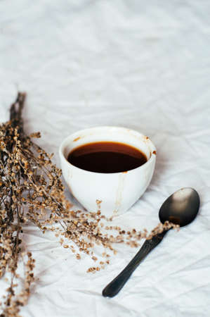 Fresh hot coffee on a pile of books on a table covered with a white cloth at the window. Still life. Rustic dark stying.の写真素材