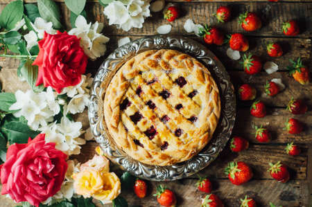 Homemade cherry and strawberry  pie on rustic background. Delicious Homemade Cherry Pie with a Flaky Crust. Rustic dark style. decorated with roses and jasmine flowers. Dessert for the familyの写真素材