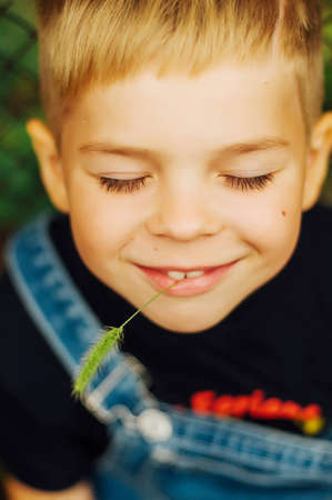 Portrait of smiling seven year old boy. Seven year old boy  with brown eyes and blond hair. Young boy in a black T-shirt and denim overalls outdoor.  Boy's portrait.の写真素材