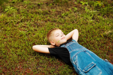 Portrait of smiling seven year old boy. Seven year old boy  with brown eyes and blond hair. Young boy in a black T-shirt and denim overalls outdoor.  Boy's portrait.の写真素材