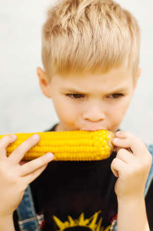 Young boy with  corn on the cob in the backyard. A  boy happy about tearing into some freshly grilled ears of corn on the cob. Child eating a corn on the cobLittle boy enjoying eating corn on the cobの写真素材