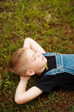 Portrait of smiling seven year old boy. Seven year old boy  with brown eyes and blond hair. Young boy in a black T-shirt and denim overalls outdoor.  Boy's portrait.の写真素材