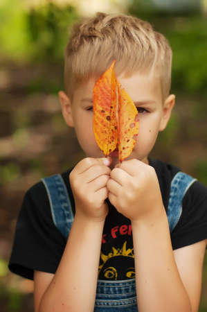Portrait of smiling seven year old boy. Seven year old boy  with brown eyes and blond hair. Young boy in a black T-shirt and denim overalls outdoor.  Boy's portrait.の写真素材