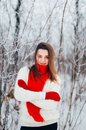 Female portrait outdoors serious expression. Young woman outside wearing warm winter clothing.  Winter portrait of young girl. Woman on the background falling snow in winter forestの写真素材