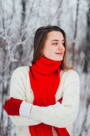 Female portrait outdoors serious expression. Young woman outside wearing warm winter clothing.  Winter portrait of young girl. Woman on the background falling snow in winter forestの写真素材