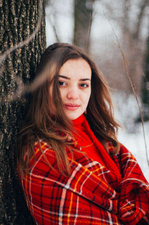 Female portrait outdoors serious expression. Young woman outside wearing warm winter clothing.  Winter portrait of young girl. Woman on the background falling snow in winter forestの写真素材
