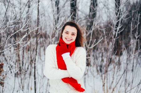Female portrait outdoors serious expression. Young woman outside wearing warm winter clothing.  Winter portrait of young girl. Woman on the background falling snow in winter forestの写真素材