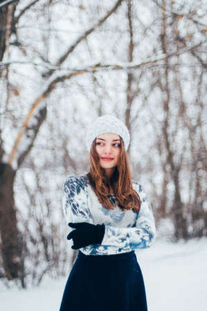 Female portrait outdoors serious expression. Young woman outside wearing warm winter clothing.  Winter portrait of young girl. Woman on the background falling snow in winter forestの写真素材