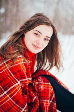 Female portrait outdoors serious expression. Young woman outside wearing warm winter clothing.  Winter portrait of young girl. Woman on the background falling snow in winter forestの写真素材
