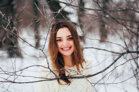 Female portrait outdoors serious expression. Young woman outside wearing warm winter clothing.  Winter portrait of young girl. Woman on the background falling snow in winter forestの写真素材