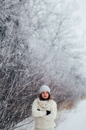 Female portrait outdoors serious expression. Young woman outside wearing warm winter clothing.  Winter portrait of young girl. Woman on the background falling snow in winter forestの写真素材