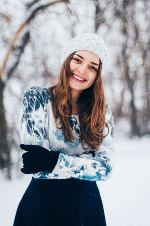 Female portrait outdoors serious expression. Young woman outside wearing warm winter clothing.  Winter portrait of young girl. Woman on the background falling snow in winter forestの写真素材
