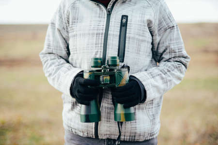 Young woman looking through binoculars on a autumn nature. Binocular, traveler, hiking.  young caucasian female hiker holding in his hand binoculars. Horizontal shape, front view,の写真素材