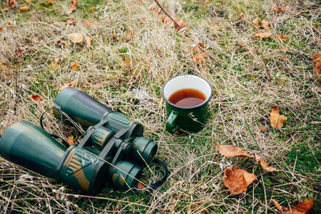 Young woman drinking tea on a autumn nature. Binocular, traveler, hiking.  young caucasian female hiker holding in his hand cuo of tea. Horizontal shape, front view,の写真素材