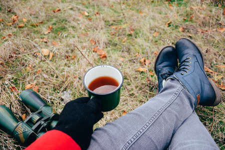 Young woman drinking tea on a autumn nature. Binocular, traveler, hiking.  young caucasian female hiker holding in his hand cuo of tea. Horizontal shape, front view,の写真素材