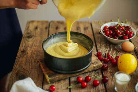 Ingredients for baking cake stuffed with fresh cherry pie. Female preparing cherry pie. Rustic dark...