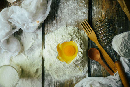 Ingredients for baking croissants - flour, wooden spoon, rolling pin, eggs, egg yolks, butter served on wooden background.の写真素材