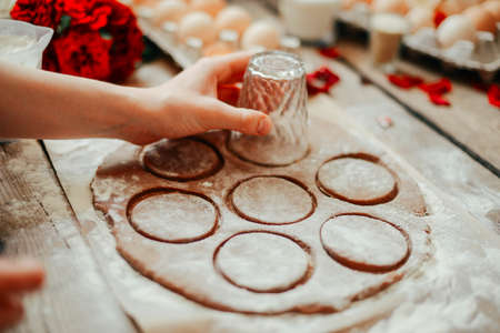hands cut cookie from raw dough on a wooden table. Healthy baking ingredients - flour,  butter, eggs, biscuits over a wooden table background.の写真素材