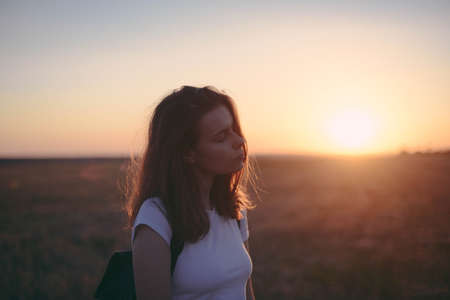 Portrait of happy and enjoying young woman on a meadow on a sunset. Cheerful girl on sunset. Lifestyle and happiness concept.の写真素材