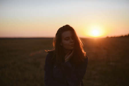 Portrait of happy and enjoying young woman on a meadow on a sunset. Cheerful girl on sunset. Lifestyle and happiness concept.の写真素材