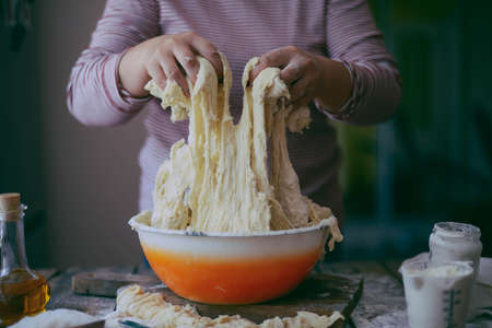 Close up view of baker kneading dough. Homemade bread. Hands preparing bread dough on wooden table. Preparing traditional homemade bread. Woman hands kneading fresh dough for making breadの写真素材