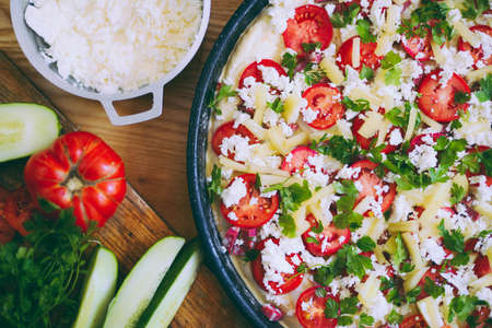Raw pizza dough with sauce and ingredients on wooden table.の写真素材