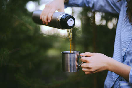 Traveler girl pouring tea from thermos cup, outdoors. Young woman drinking tea at cup. Theme travel....