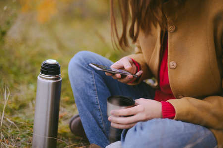 Traveler girl pouring tea from thermos cup, outdoors. Young woman drinking tea at cup. Theme travel....