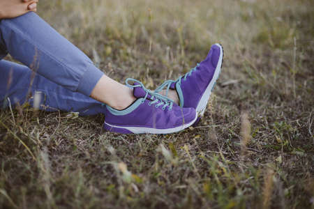 Sport concept,blue sneakers for running  with walkgirlslying on grass. Girl sitting on pitch, no face, legs in professional sport shoes, closeup. Outdoors, sunlight, fieldの写真素材