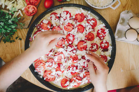 Raw pizza with sauce and ingredients on wooden table. Fresh o raw pizza, preparation in traditional style. Margherita pizza with utensils and vegetable on slate plateの写真素材