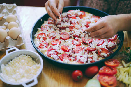 Raw pizza dough with sauce and ingredients on wooden table. Fresh o raw pizza, preparation in traditional style. Margherita pizza with utensils and vegetable on slate plateの写真素材