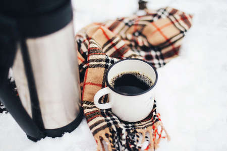 woman hands pours hot tea or coffee out of  flask on winter forest background.