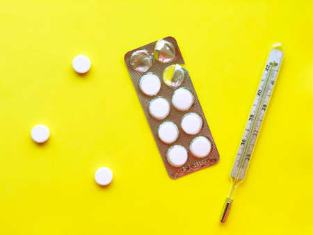 Pills, thermometer on a yellow background, top view. 