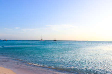 Ocean with blue water and fine sand. On the garisont, boats and yachts are visible. The sun at...