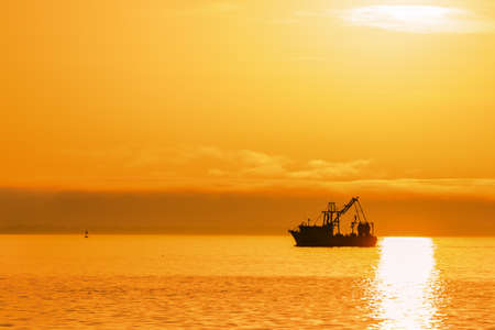 Silhouetted fishing boat on ocean with sunsetの写真素材