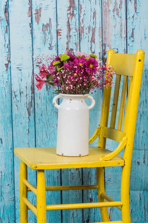 Bouquet of flowers in vintage vase sitting on yellow chairの写真素材